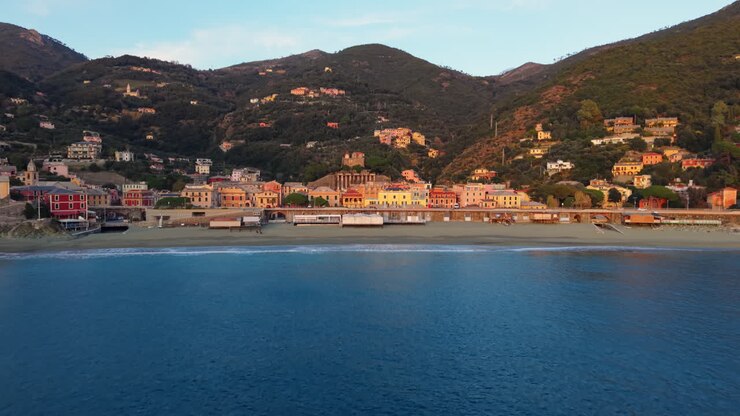 Il drone si muove dal mare verso il villaggio di Bonassola con edifici costieri e colline.