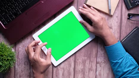 persona usando una tableta con una pantalla verde en un escritorio de madera
