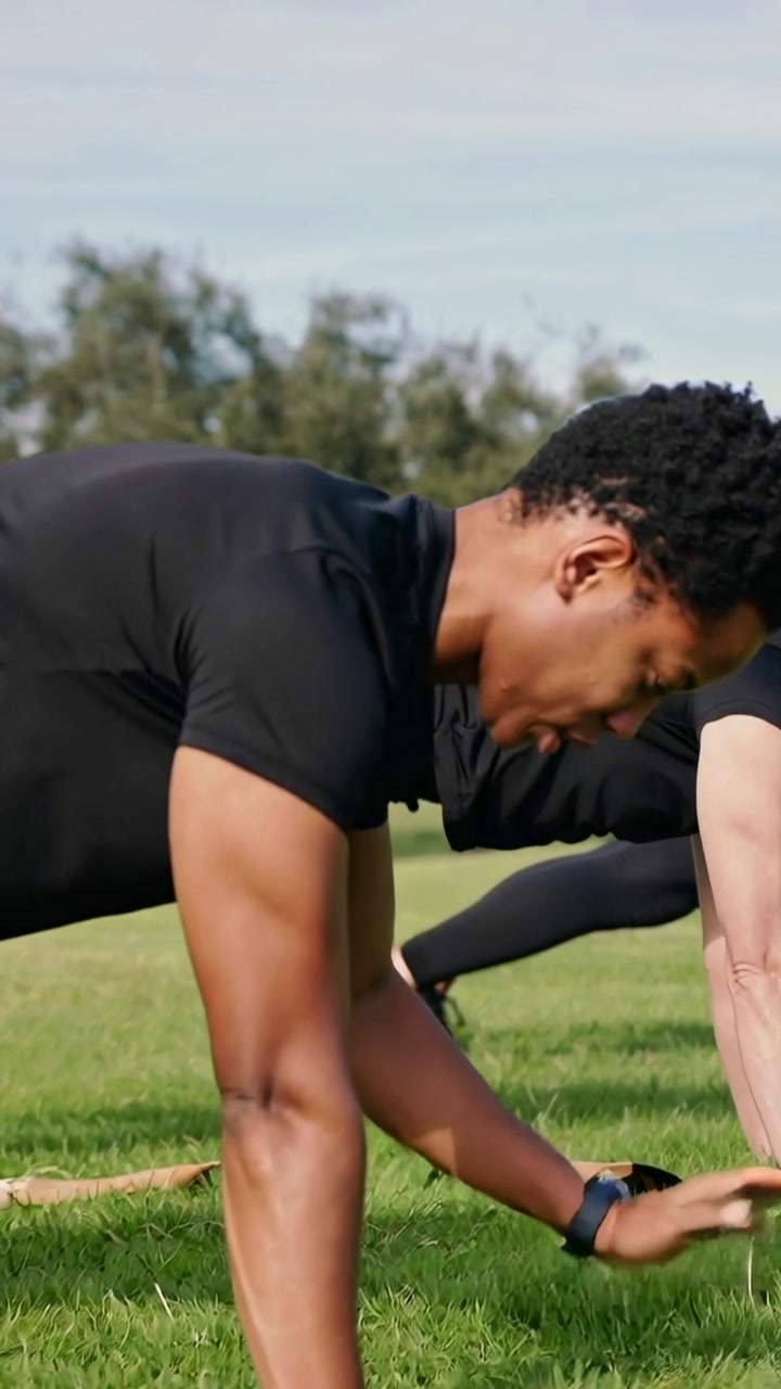 Vertical video: Holding plank, man in black shirt alternating reaches on mat in park for core