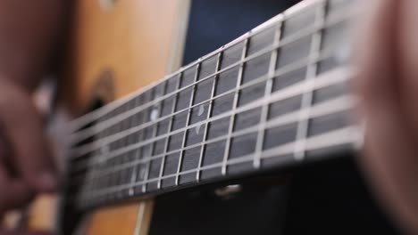 extreme close-up of strumming a guitar panning over to the other hand on the fret board