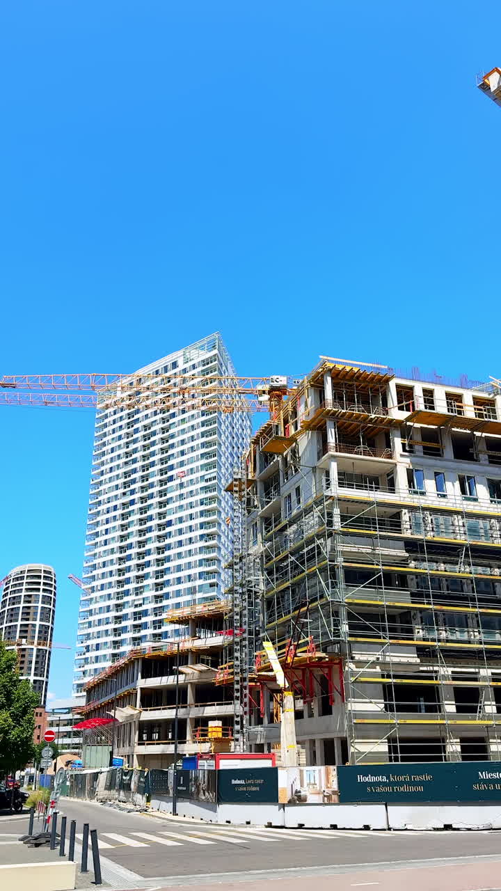 New construction project in urban area. Workers are busy erecting a large building with cranes and scaffolding under a clear blue sky in a bustling city