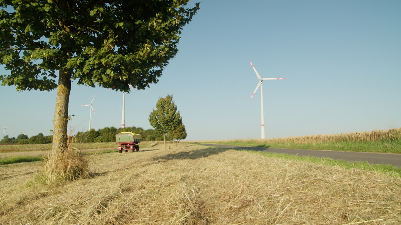 A single wind turbine stands tall near a quiet country road and harvested farmland under a clear summer sky, symbolizing clean energy in agriculture