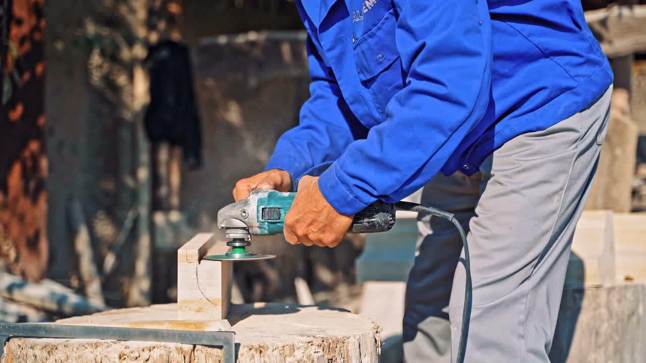 Stone processing from rock. Worker in gloves with a small angle grinder cuts a granite slab