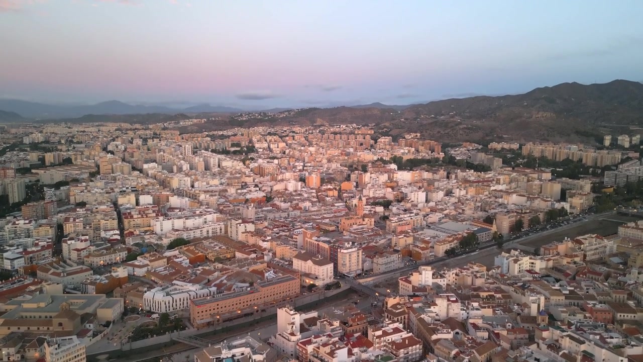 Pemandangan udara tinggi yang mendongak ke atas kota Malaga dan sekitarnya di bawah langit matahari terbit yang bersinar. Direkam dalam 4K pada 25 fps