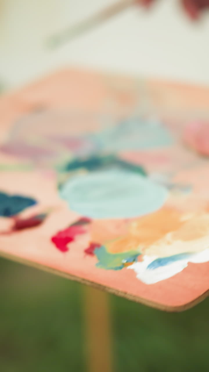 체크색 셔츠를 입고 얼굴이 보이지 않는 예술가 한 명이 화려한 색으로 가득 찬 페인트 브러쉬와 패을 들고 있습니다. 흐릿한 배경은  캔버스를 드러니다.