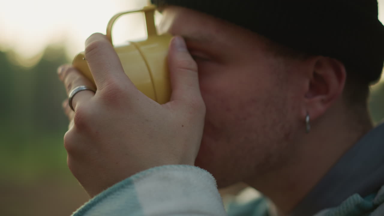 Escursionista che si gode un momento di pace, uomo beve durante l'ora dorata nella foresta, uomo tranquillo con tazza fumante nel bosco, uomo pensieroso si rilassa con una bevanda calda tra i tranquilli pini al tramonto