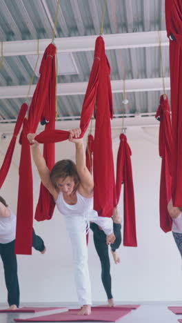 flexible women stand on one leg holding fly yoga hammock above head and practicing asana low angle shot close view