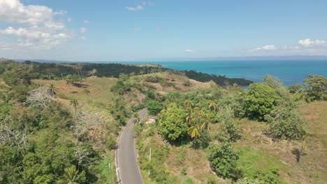 Aerial-flyover-road-with-driving-car-in-rural-area-of-Sabana-de-la-Mar,-Dominican-Republic-and-Blue-Caribbean-Sea-in-background