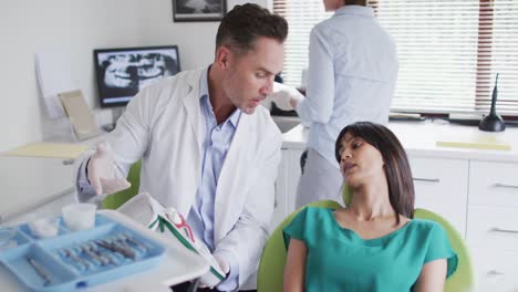 Caucasian-male-dentist-with-dental-nurse-examining-teeth-of-female-patient-at-modern-dental-clinic