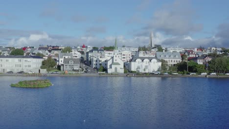 volando hacia la icónica iglesia fríkirkjan í reykjavík sobre el lago tjörnin, islandia