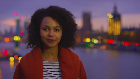 portrait of woman against city lights of london and the river thames outdoors wearing winter coat at dusk - shot in slow motion