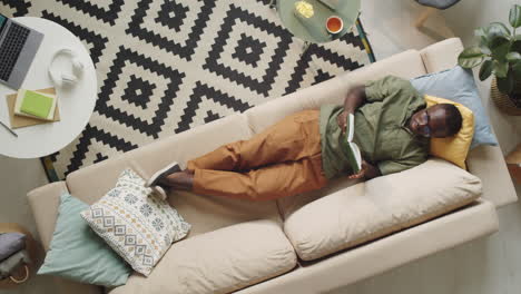 black man lying on sofa and reading book