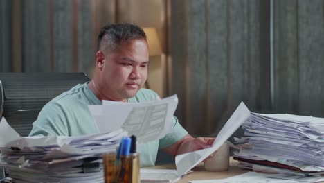 close up of fat asian man with laptop drinking water while working hard with documents at the office