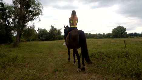 girl rides on horseback at daytime view from behind