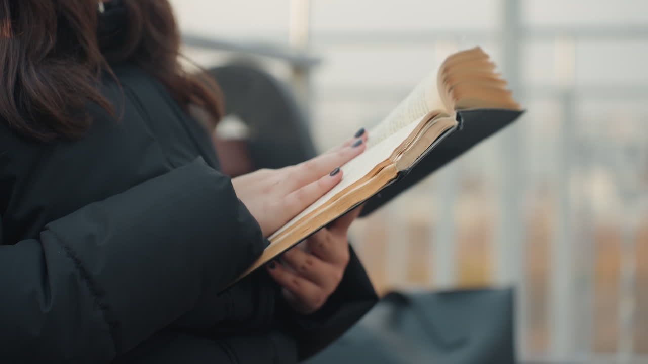 Woman reads evening. Woman enjoying peaceful book reading on urban rooftop during twilight. Casual woman immerses herself in book while relaxing on rooftop at dusk with city skyline blurred