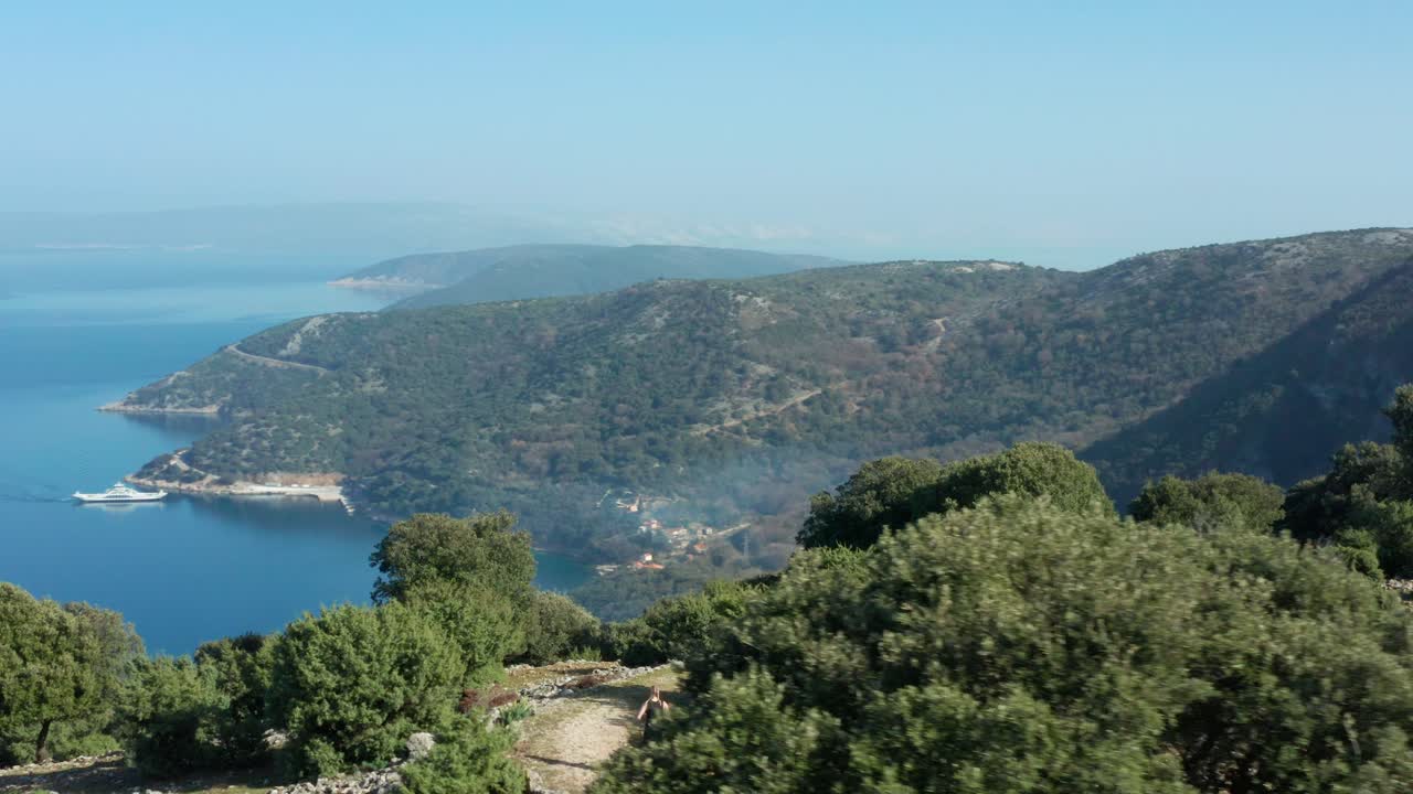 hombre con perro mascota corriendo por un sendero de montaña con vistas al mar adriático en la isla de cres, croacia