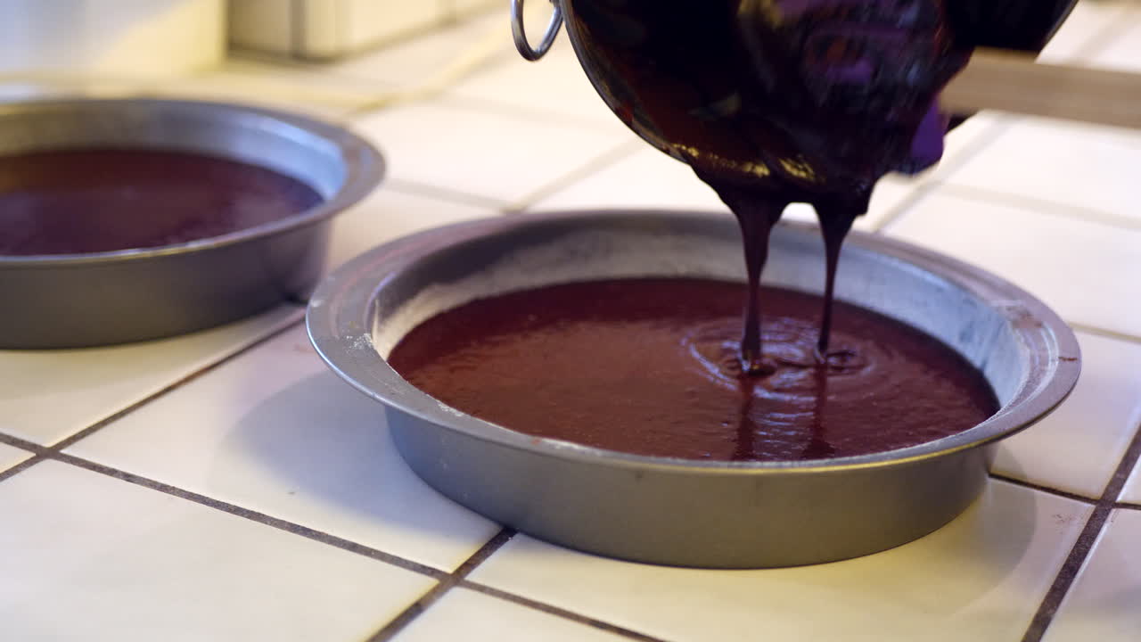 A chef in the kitchen pouring and scooping delicious vegan chocolate cake batter into a round baking pan with a rubber spatula