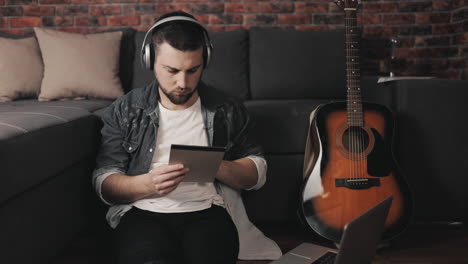 young musician man listening to music with laptop and wireless headphones taking notes at home 1