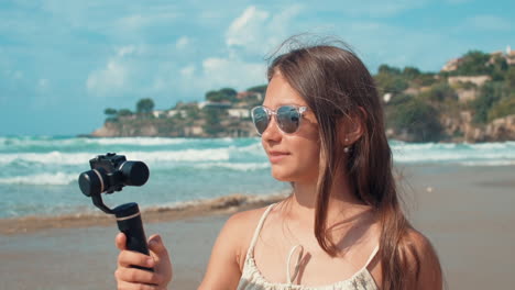 Young-woman-recording-video-outdoor.-Joyful-vlogger-girl-looking-camera-at-beach