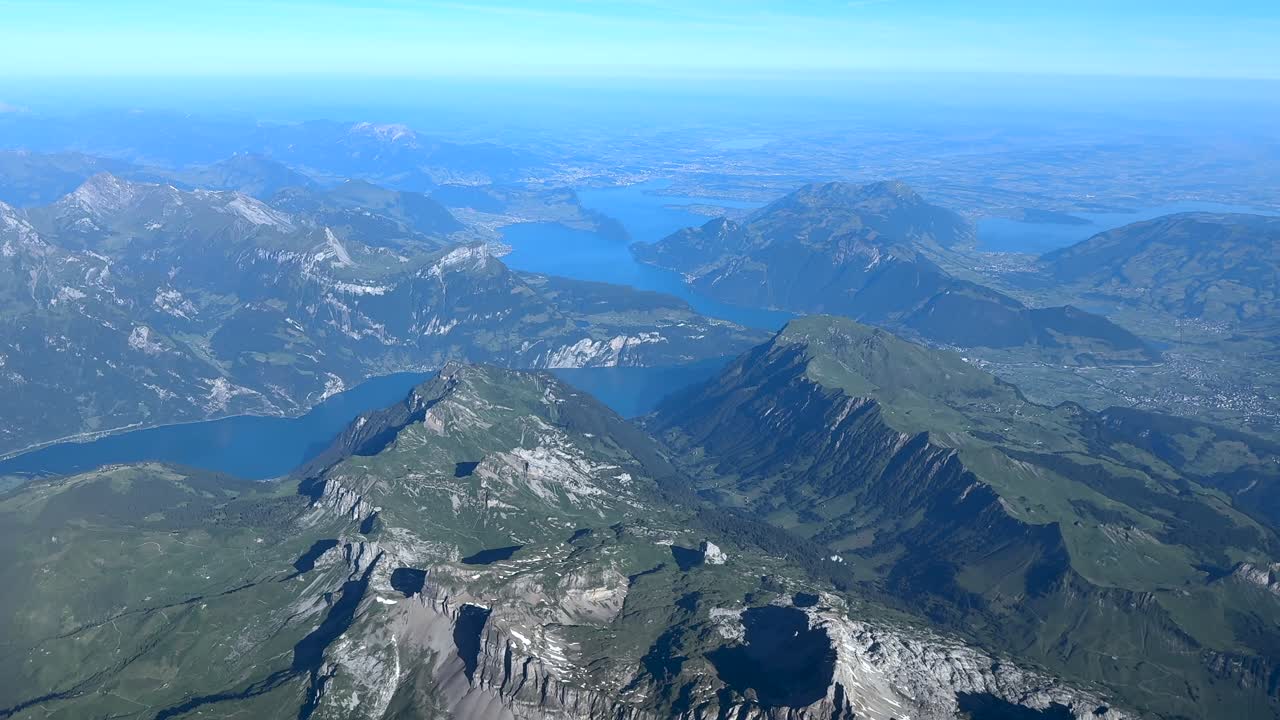 An aerial cockpit view flying above the Swiss Alps Mountains in a hazy summer morning under a brigh morning light.