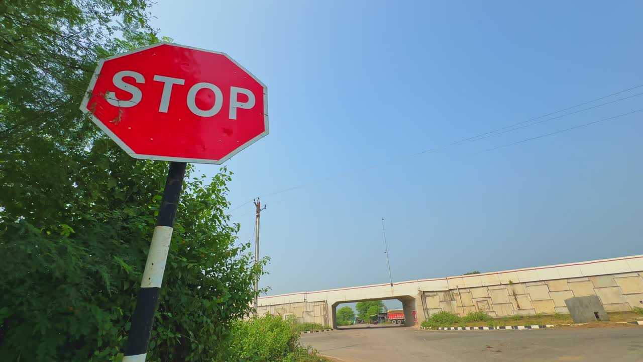 Camera slowly circles around a red stop sign near a rural road and overpass on a clear sunny day