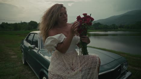 woman with flowers by vintage car by lake