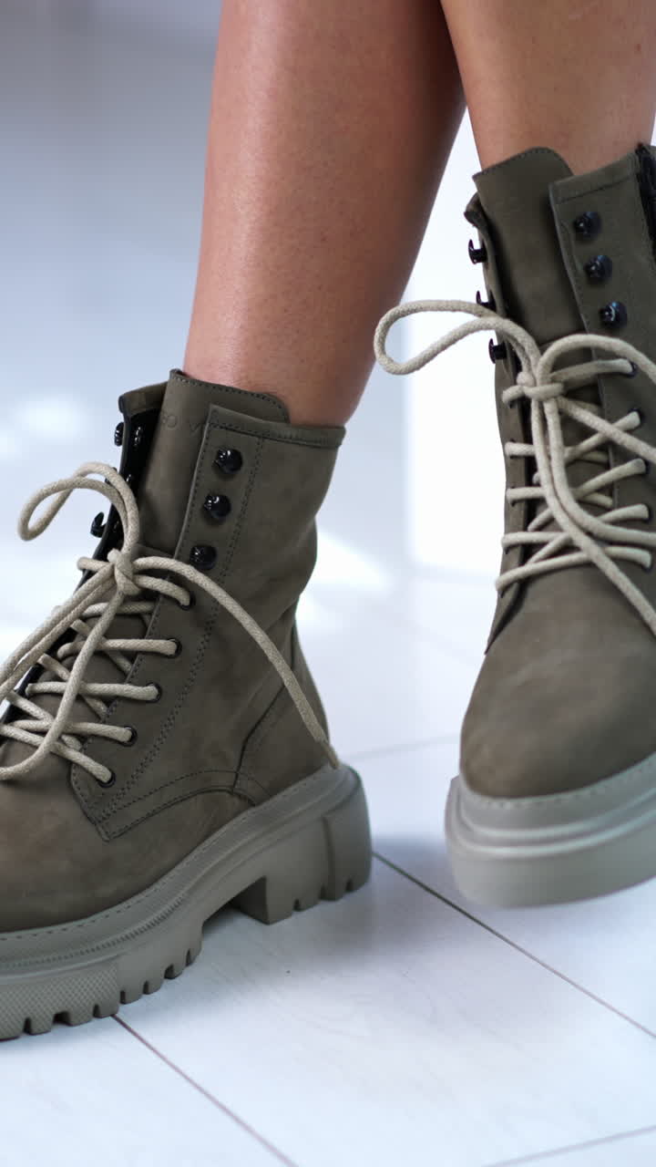 Model ties the laces on the modern boots. Sitting female demonstrating grey fashionable footwear. Close up. Vertical video