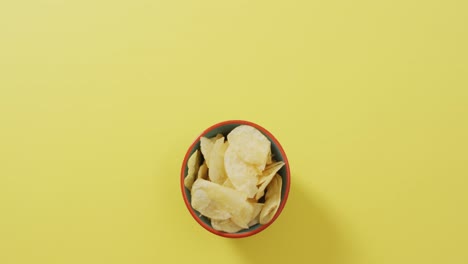 close up of potato chips in a bowl with copy space on yellow surface