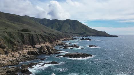 las olas chocan contra los acantilados con vistas a las montañas en el fondo cerca de big sur, california