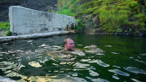 man swimming on the iconic outdoor pool of seljavallalaug in southern iceland