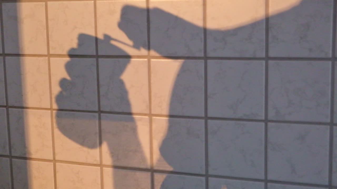 전통적인 수동 커피 그라인더를 사용하는 남자의 그림자가 있는 주방 타일 벽