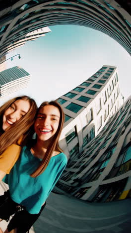 two young women smiling and taking a wide-angle selfie in the city