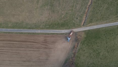 top down aerial footage of a farmer starting to prepare a dry field in a blue tractor