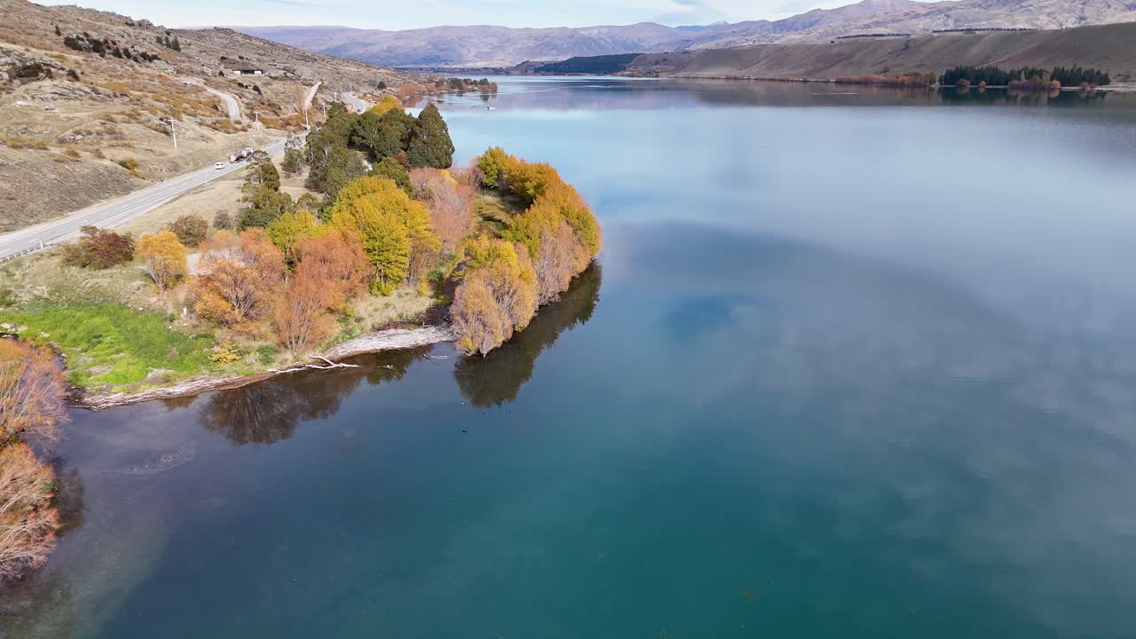 Drone footage captures Lake Dunstan's serene waters and vibrant autumn foliage in Cromwell, New Zealand, under soft natural lighting