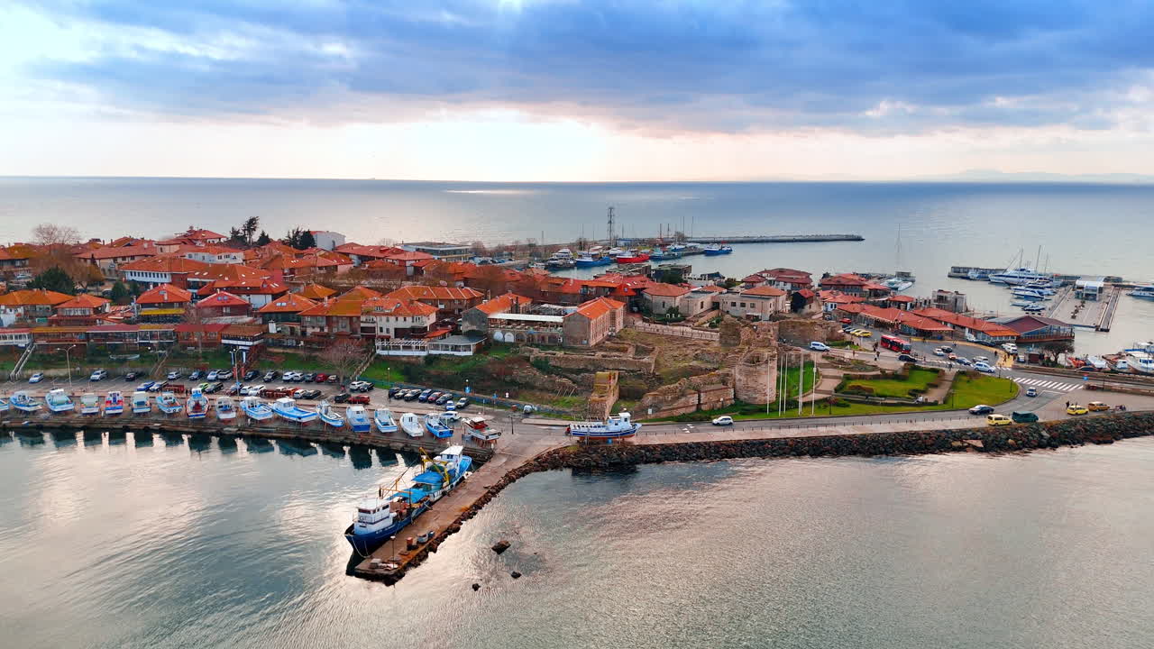 Veduta aerea di un porto peschereccio e rovine antiche sul mare. Veduta dall'alto di un porto con barche blu e rovine medievali in pietra vicino alla costa.