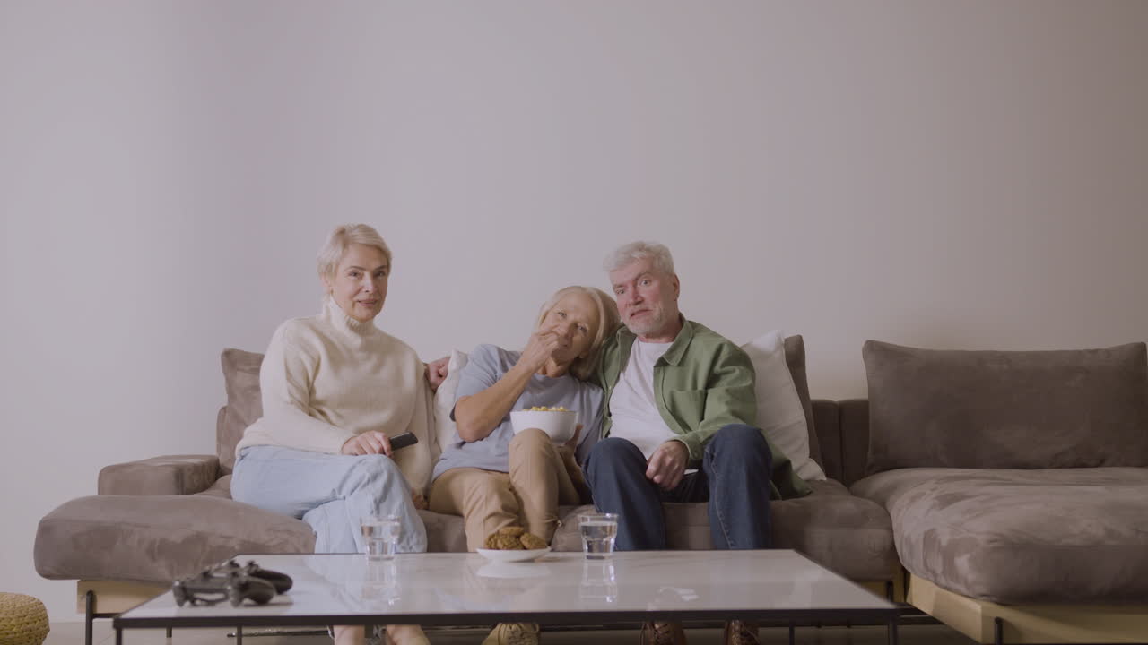 Group Of Three Senior People Watching Tv While Sitting On Sofa At Home