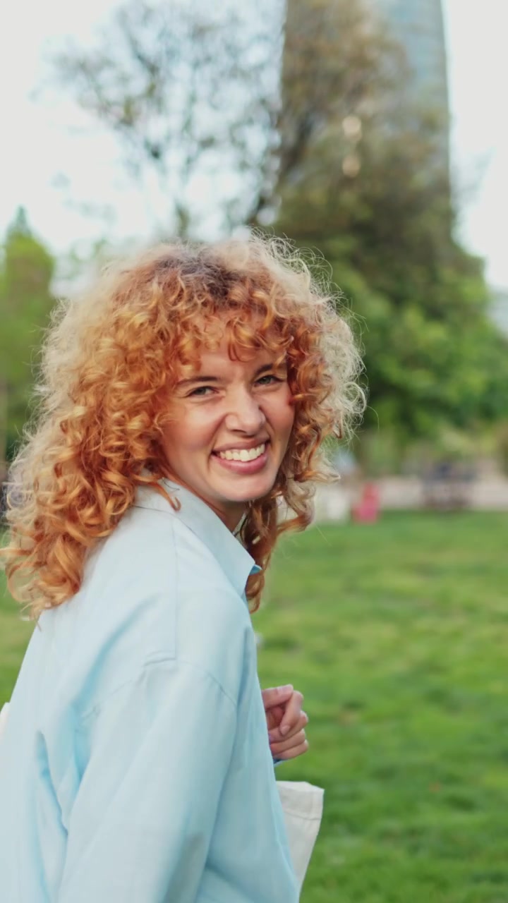 Smiling Young Woman with Curly Red Hair Walking in Park
