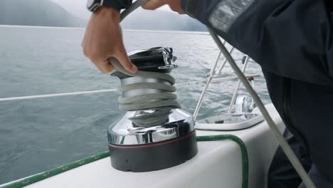 Close-Up-of-Male-Hands-Wrapping-Sailboat-Rope-Around-Winch-With-Cold-Ocean-Scene-in-Background,-Slow-Motion