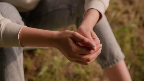 close-up of individual hands clasping together in a calm, reflective pose, resting on knees with soft background of autumn foliage on ground