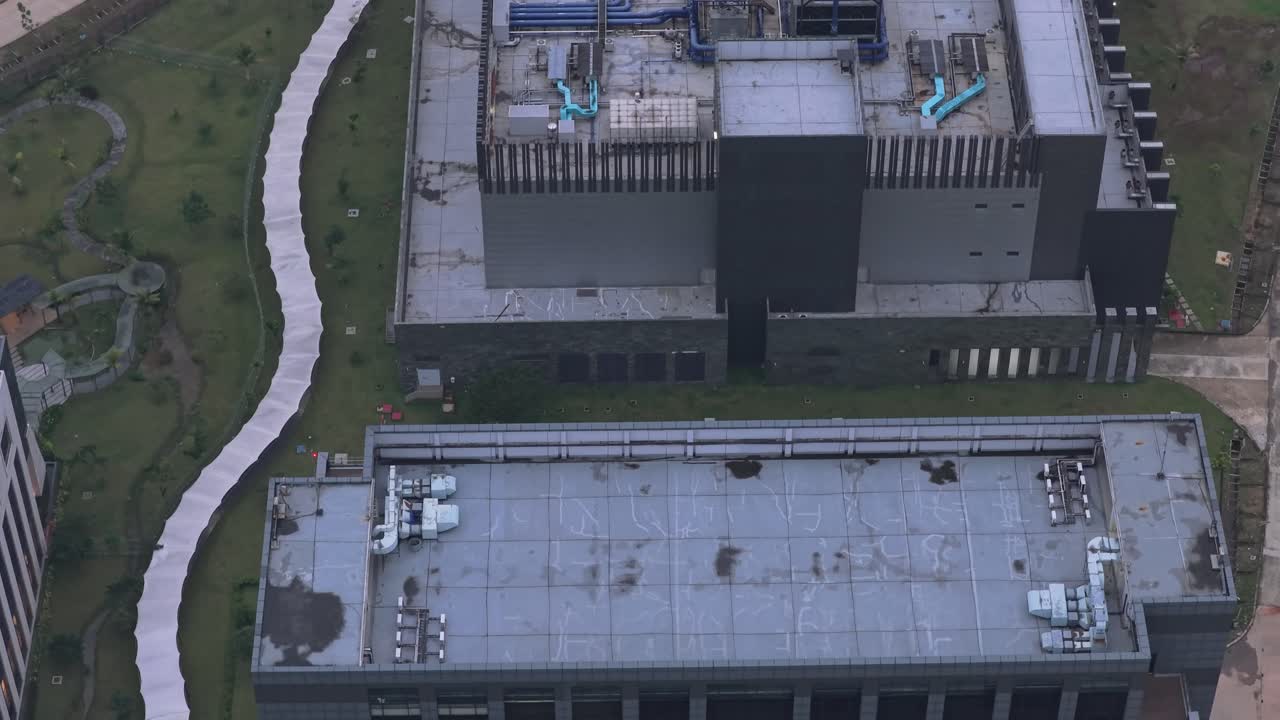 High angle view of a modern data center building surrounded by green space. The camera slowly reveals the rooftop with its cooling systems