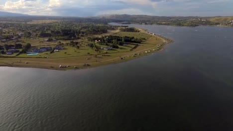 aerial drone footage of a car moving in the lake shore with mountains in the background