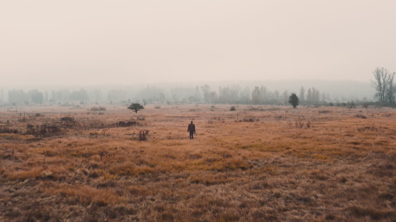 A documentarist with a camera walking in a brown misty autumn field