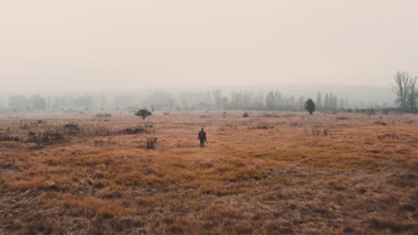 a documentarist with a camera walking in a brown misty autumn field