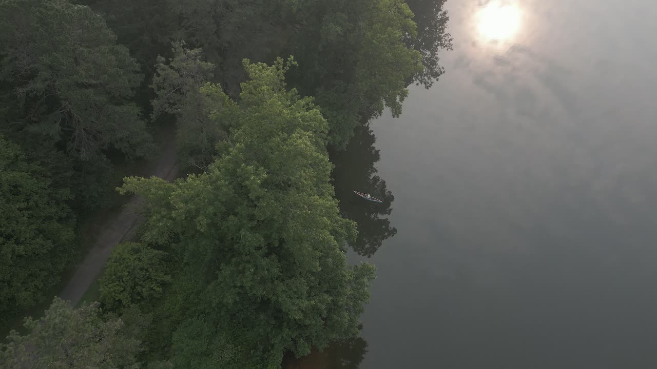 Aerial view: Lone person paddles canoe away from shore on foggy lake