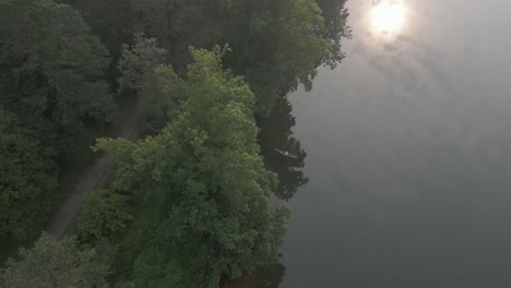 aerial view: lone person paddles canoe away from shore on foggy lake
