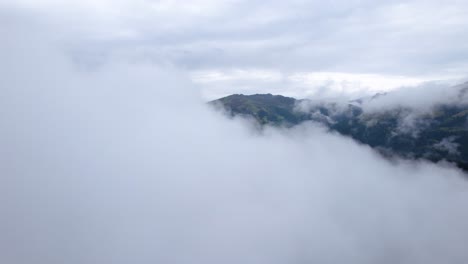 drone flying over a thin layer of clouds towards a mountain landscape