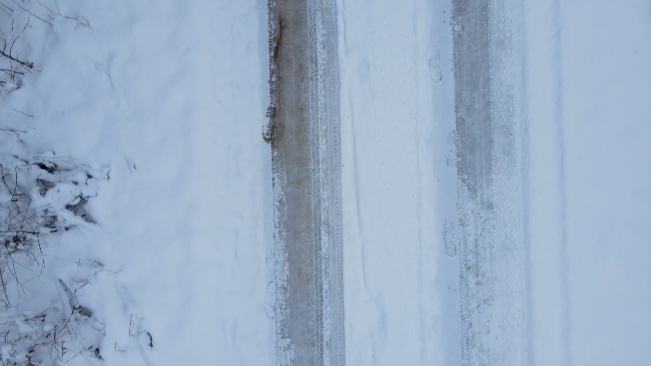 눈 속에서 타이어의 트레드마크가 있는 숲의 눈 덮인 진흙길의 공중 낮은 각도