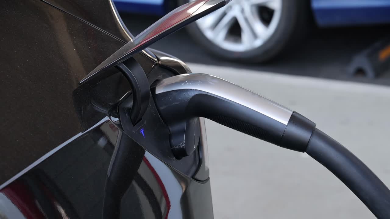 Close-up sequence of a hand plugging a charger into an electric car's charging port.