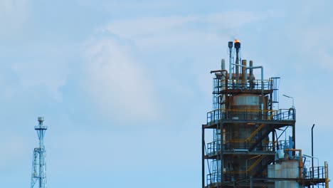 Slow-motion-shot-of-large-industrial-refinery-with-fire-and-black,-polluting-smog-pouring-out-the-top-into-a-clear-blue-sky-in-Curacao