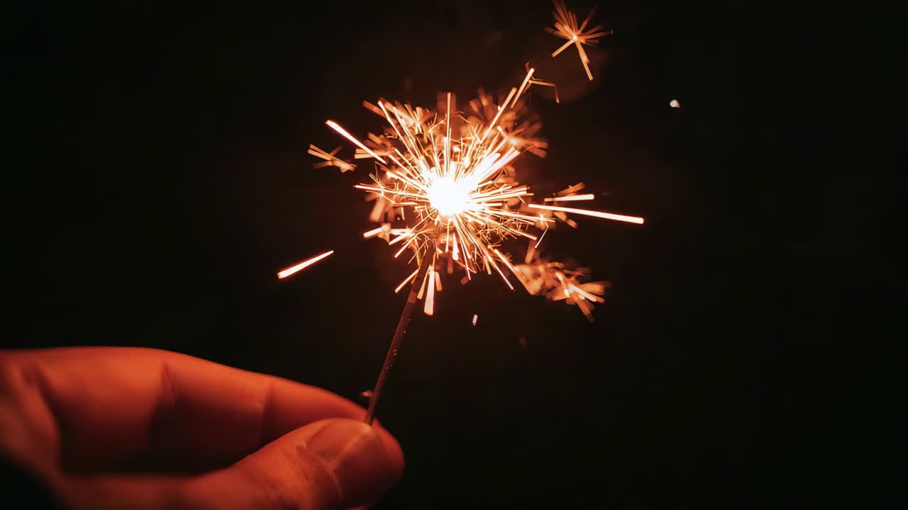 Mano di adulto che accende una stella filante ed emette scintille arancioni brillanti di notte, con scia di fumo